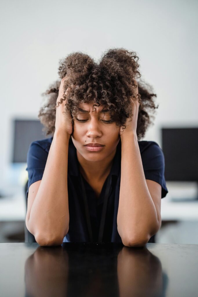 pexels-photo-12912159-12912159 Woman in office setting expresses stress, seated at desk with hands in hair. Perfect for workplace stress concept.