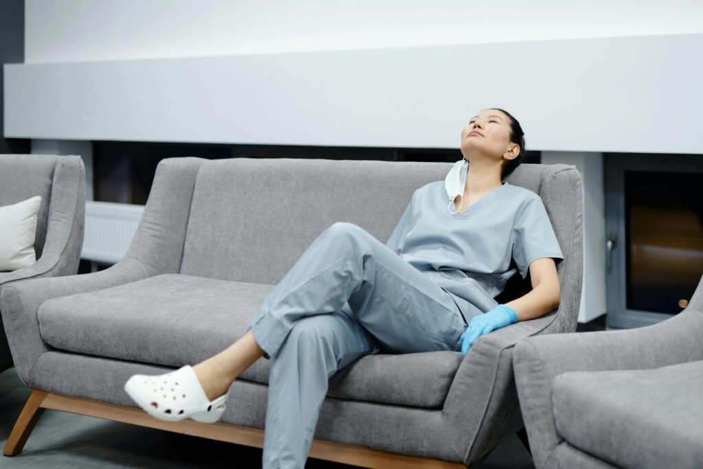 pexels-photo-4270365-4270365-1 Nurse in scrubs takes a break, resting on a comfy hospital couch after a long shift.